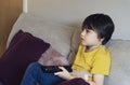 Portrait kid sitting on sofa holding remote control, Candid short a happy child boy relaxing at home watching TV , Activity for