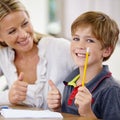 Portrait, kid and teacher with thumbs up in classroom, smile and pencil. Happiness, educator and student with hand