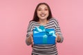 Portrait of kind generous woman in striped sweatshirt smiling joyfully and giving birthday gift to camera