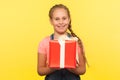 Portrait of kind merry little girl with braid holding gift box and smiling to camera, child enjoying birthday present Royalty Free Stock Photo