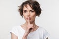 Portrait of kind woman with short brown hair in basic t-shirt holding index finger on lips