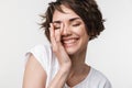 Portrait of kind woman with short brown hair in basic t-shirt smiling and touching her face with hand