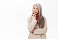 Portrait of korean businesswoman, woman with grey hair thinking, wearing suit, smiling intrigued, standing over white Royalty Free Stock Photo