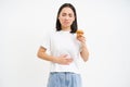 Portrait of korean woman has stomach ache, touching belly, holding cupcake, cant eat pastry, white studio background