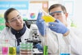 Laboratory workers man and woman examine yellow liquid in flask. Royalty Free Stock Photo