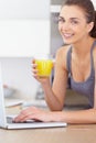 Portrait, laptop and smile for orange juice with a woman in the kitchen of her home to relax in the morning. Computer