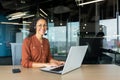 Portrait of Latin American business woman, office worker looking at camera and smiling, using headset and laptop for Royalty Free Stock Photo