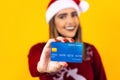 Portrait of Latin woman holding a credit card for shopping at Christmas wearing a santa hat on yellow background in Mexico latin A Royalty Free Stock Photo