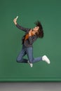 Portrait of Latino beautiful girl jumping and using phone isolated on green, vintage color studio background. Concept of