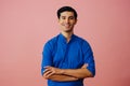 Portrait latino man with arms crossed and black hair smiling handsome young adult blue shirt over pink background