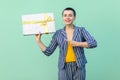 Portrait of laughing beautiful with short hair young woman in striped suit standing, holding present box and pointing finger to it Royalty Free Stock Photo