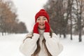 Portrait of laughing girl in red knitted hat and mittens and woolen sweater on alley in winter park