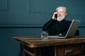 Portrait of laughing gray-haired mature older business man talking on mobile phone sitting at table with laptop computer Royalty Free Stock Photo