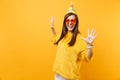 Portrait of laughing happy young woman in orange heart glasses, birthday party hat spreading hands isolated on bright