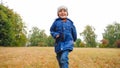 Portrait of laughing little boy running on grass at field on cloudy autumn day Royalty Free Stock Photo