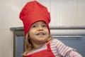 Portrait of a laughing little girl in a red chef`s hat and apron in the kitchen. Royalty Free Stock Photo