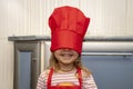 Portrait of a laughing little girl in a red chef`s hat pulled over her eyes and an apron. Royalty Free Stock Photo