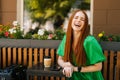 Portrait of laughing redhead young woman sitting at table with coffee cup and mobile phone in outdoor cafe terrace in Royalty Free Stock Photo