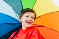 Portrait of a laughing school boy with rainbow umbrella behind. Smiling kid holds colourful umbrella on his shoulder Royalty Free Stock Photo
