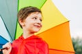 Portrait of a laughing school boy with rainbow umbrella behind. Smiling kid holds colourful umbrella on his shoulder Royalty Free Stock Photo