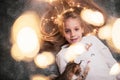 Portrait of a laughing 6 year old blonde lying on a gray background. Next to her is blurred bokeh from a festive garland Royalty Free Stock Photo