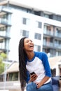 Laughing young african woman sitting outdoors with cellphone in the city Royalty Free Stock Photo