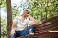 Laughing young man sitting outdoors on bench and using mobile phone Royalty Free Stock Photo