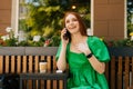 Portrait of laughing young woman talking by mobile phone, sitting at table with coffee cup in outdoor cafe terrace in Royalty Free Stock Photo