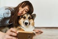 Portrait laughting young woman hugging cute Welsh Corgi dog dog and taking selfie with pet on smartphone camera.