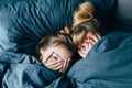 Portrait of light hair long hair mother and daughter under the duvet together in soft morning light on blue linen bed. Concept of