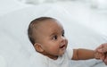 Portrait of little adorable African newborn baby sitting on bed and looking with bright eyes and smiling and holding mother hands Royalty Free Stock Photo