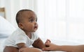 Portrait of little adorable African newborn baby sitting on bed and looking with bright eyes and smiling and holding mother hands Royalty Free Stock Photo