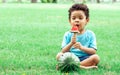 Portrait of little african curly hair cute boy playing, eating piece of watermelon with happiness while sitting on the green field Royalty Free Stock Photo