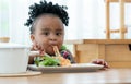 Portrait of little African hungry toddler girl eating spaghetti and vegetables with fork in kitchen at home. Happy messy preschool Royalty Free Stock Photo