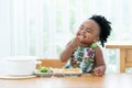 Portrait of little African hungry toddler girl eating spaghetti and vegetables with hand in kitchen at home. Happy messy preschool Royalty Free Stock Photo