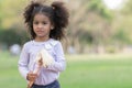 Portrait of little African kid girl with twin tails hair smiling and holding a doll in her hands at park Royalty Free Stock Photo