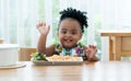 Portrait of little African toddler girl smiling while eating spaghetti and vegetables with hand in kitchen at home. Happy messy Royalty Free Stock Photo