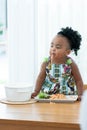 Portrait of little African toddler girl smiling while eating spaghetti and vegetables with hand in kitchen at home. Happy messy Royalty Free Stock Photo
