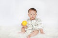 Portrait of little Asian baby boy in pajamas holding yellow plastic toy ball sitting on white fur against white background Royalty Free Stock Photo