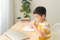 Portrait of little Asian boy drinking water while using laptop, sitting at desk and doing homework. E-learning and education Royalty Free Stock Photo