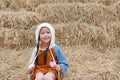 Portrait of little Asian child girl put on hood on head sitting on pile of straw