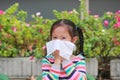 Portrait little Asian girl blowing her nose with tissue paper sitting outdoor Royalty Free Stock Photo