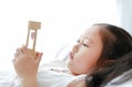 Portrait of little Asian girl looking at hourglass in hand lying on bed at home. Waiting times with sandglass. Close-up shot