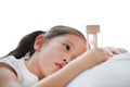 Portrait of little Asian girl looking at hourglass in hand lying on bed at home. Waiting times with sandglass. Close-up shot