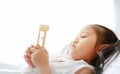 Portrait of little Asian girl looking at hourglass in hand lying on bed at home. Waiting times with sandglass. Close-up shot