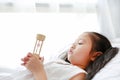 Portrait of little Asian girl looking at hourglass in hand lying on bed at home. Waiting times with sandglass Royalty Free Stock Photo