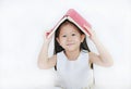 Portrait of little Asian girl place hardcover book on her head and looking camera over white background Royalty Free Stock Photo