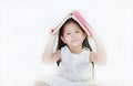 Portrait of little Asian girl place hardcover book on her head and looking camera over white background Royalty Free Stock Photo