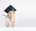 Portrait little Asian girl is wearing graduate hat holding pencil sitting thinking something and smile with happiness select focus Royalty Free Stock Photo