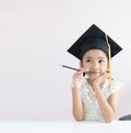 Portrait little Asian girl is wearing graduate hat holding pencil sitting thinking something and smile with happiness select focus Royalty Free Stock Photo